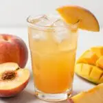 Peach mango dirty soda recipe in a glass with tropical fruit garnish