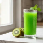 kiwi juice recipe in a clear glass with fresh kiwi slices on a marble surface