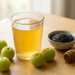 Freshly made nelli fruit juice in a glass with green nelli fruits and black salt on a wooden surface