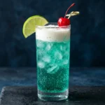 Dirty Baja Blast recipe in a tall glass with teal soda, white coconut cream float, lime wedge, and maraschino cherry garnish