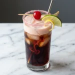 Dirty cherry coke soda recipe in a tall glass with ice, cream float on top, and a maraschino cherry garnish