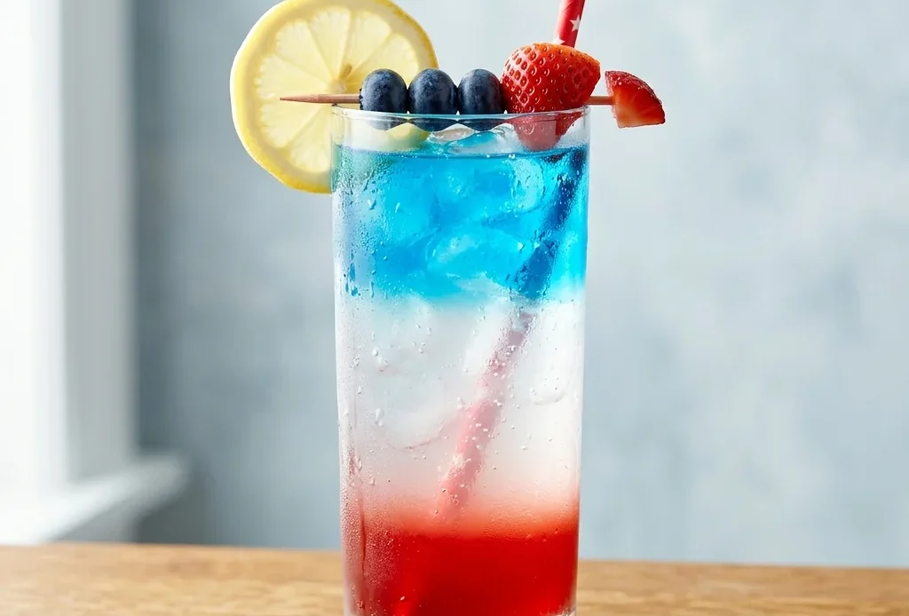 layered 4th of july mocktail in tall clear glass with red white and blue layers lemon wheel and strawberry garnish