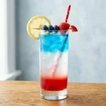 layered 4th of july mocktail in tall clear glass with red white and blue layers lemon wheel and strawberry garnish