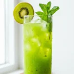 Kiwi juice recipe in a glass with ice and mint, kiwi slice on rim, on a bright white surface
