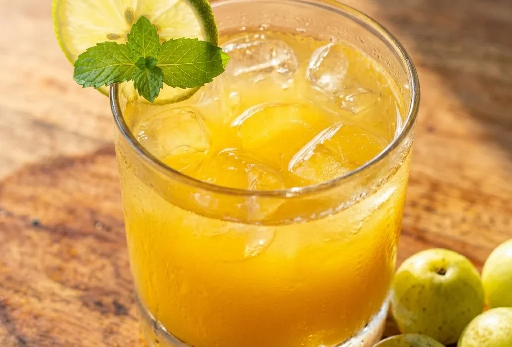 nelli fruit juice recipe in a rocks glass with lime wheel and fresh amla on a wood surface
