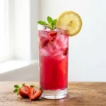 strawberry iced tea recipe in a tall Collins glass with lemon wheel and fresh strawberry garnish, condensation, warm wood surface
