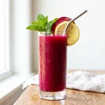 Beet juice recipe in a tall glass with lemon and mint garnish