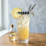Lavender syrup in a glass bottle beside a glass of iced lavender lemonade with lemon and dried lavender