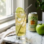 Olipop caramel apple copycat in a tall glass next to an OLIPOP Caramel Apple can and a green apple