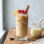 Spanish latte in a tall glass with layers of espresso and milk over ice beside a small jar of condensed milk