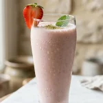 Glass of strawberry lassi recipe garnished with strawberry and cardamom